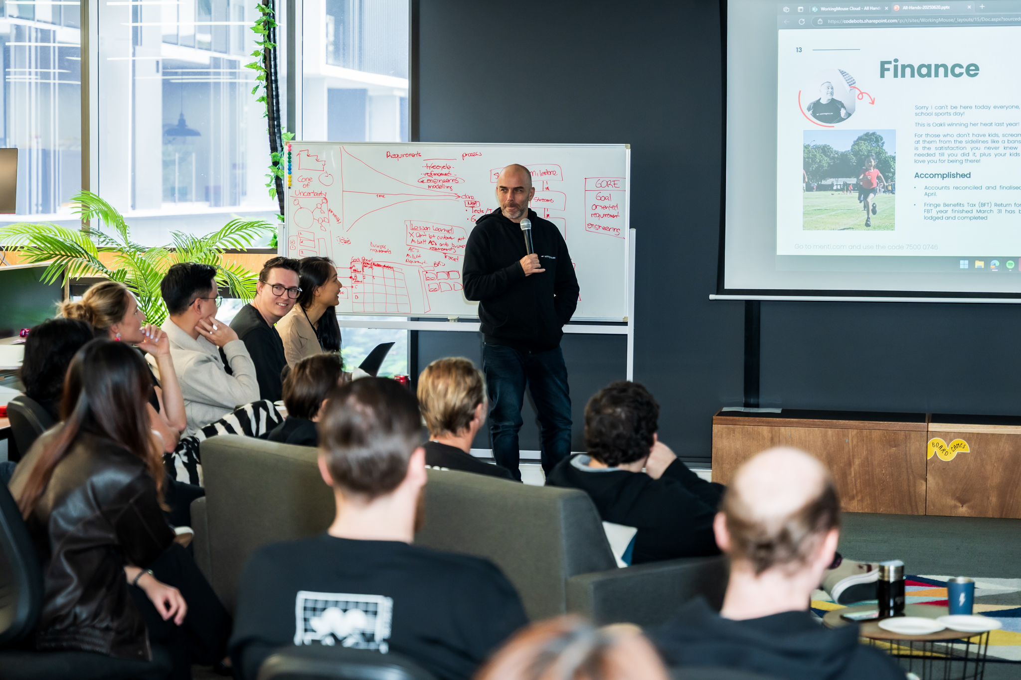 Eban speaking to a room while presenting beside a whiteboard and projection screen.