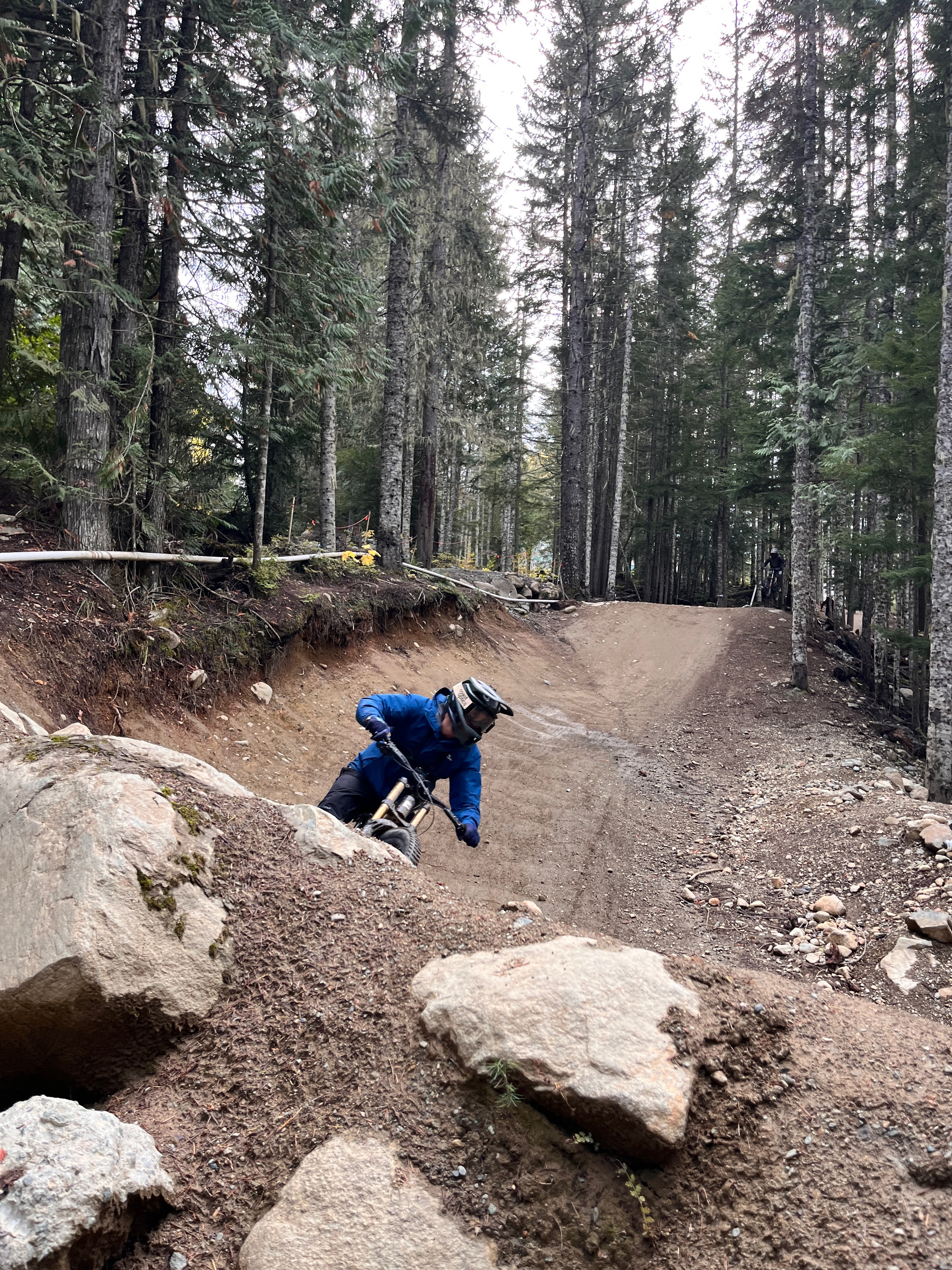 Eban mountain biking low through a berm on a forest trail.